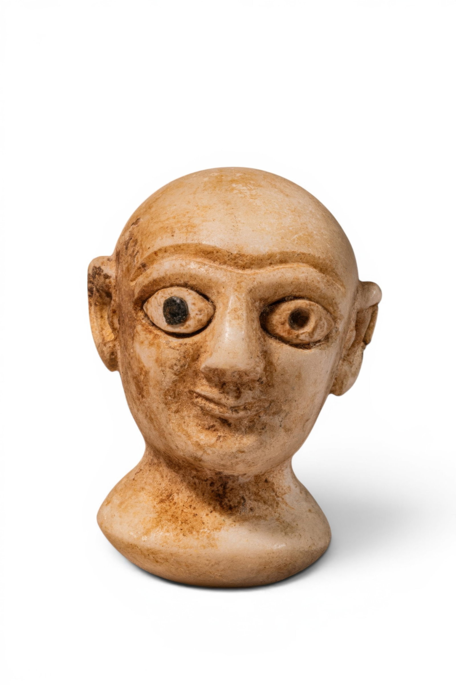 MESOPOTAMIAN MARBLE HEAD OF PRIEST WITH INLAID EYES: Ca. 2500 - 2000 BC. A marble head of a priest with a bald cranium, rounded face, and prominent almond-shaped eyes with dark inlays. The brows are carved as a continuous arched ridge above the long str