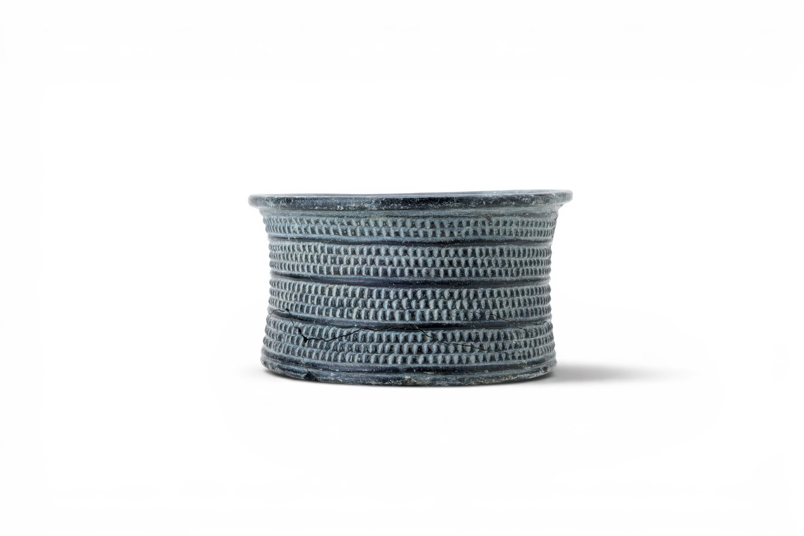 BACTRIAN CHLORITE BOWL: Ca. 3000 - 2500 BC. A chlorite bowl with a cylindrical body, thick everted rim, deep plain interior, and flat circular base. The exterior is carved with four horizontal registers of closely spaced squ