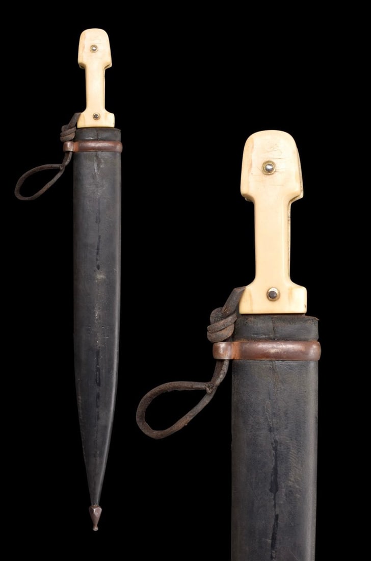 CAUCASIAN STEEL DAGGER (KINDJAL) WITH LEATHER SCABBARD: Ca. 1330H (AD 1911). A steel dagger commonly referred to as a kindjal. Whilst the bone handle is of a type commonly found in the Caucasus, the blade bears an Arabic makers mark. As such, this item is 