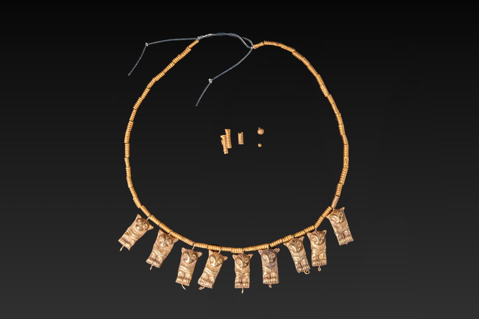 STUNNING EARLY GREEK GOLD NECKLACE WITH LION-SHAPED PENDANTS: Ca. 1200 - 800 BC. A gold necklace restrung with nine sheet-gold pendants in the form of lions shown frontally, each suspended from a collar of ribbed tubular beads. Each animal plaque is modelled in 