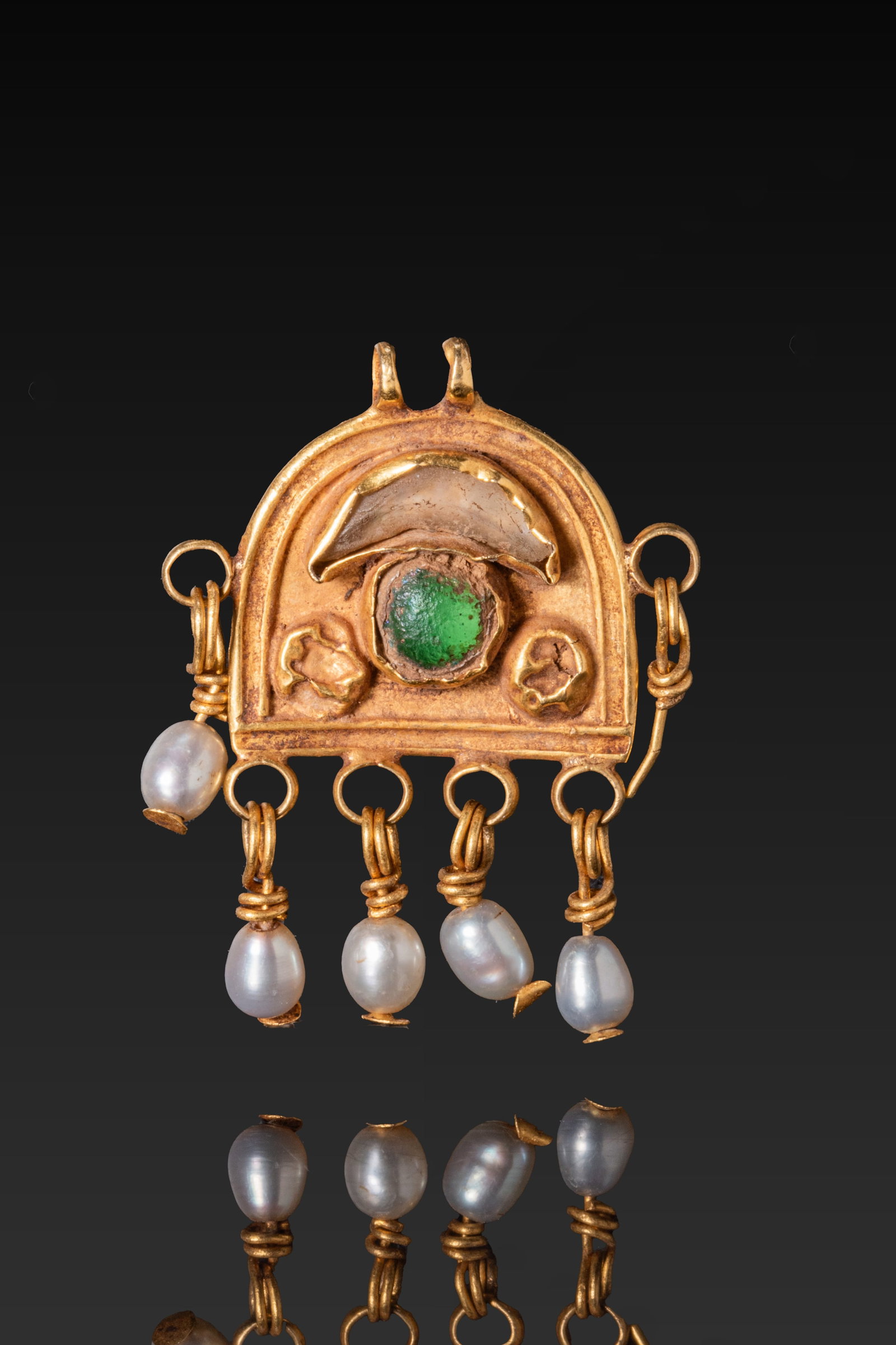 BYZANTINE GOLD AND PEARL PENDANT WITH GREEN GLASS INSET: Ca. AD 600. A gold pendant with an arched plaque and a central green glass inset, mounted below a translucent glass crescent and between two bosses. Raised borders enclose the plaque, with pearl drops