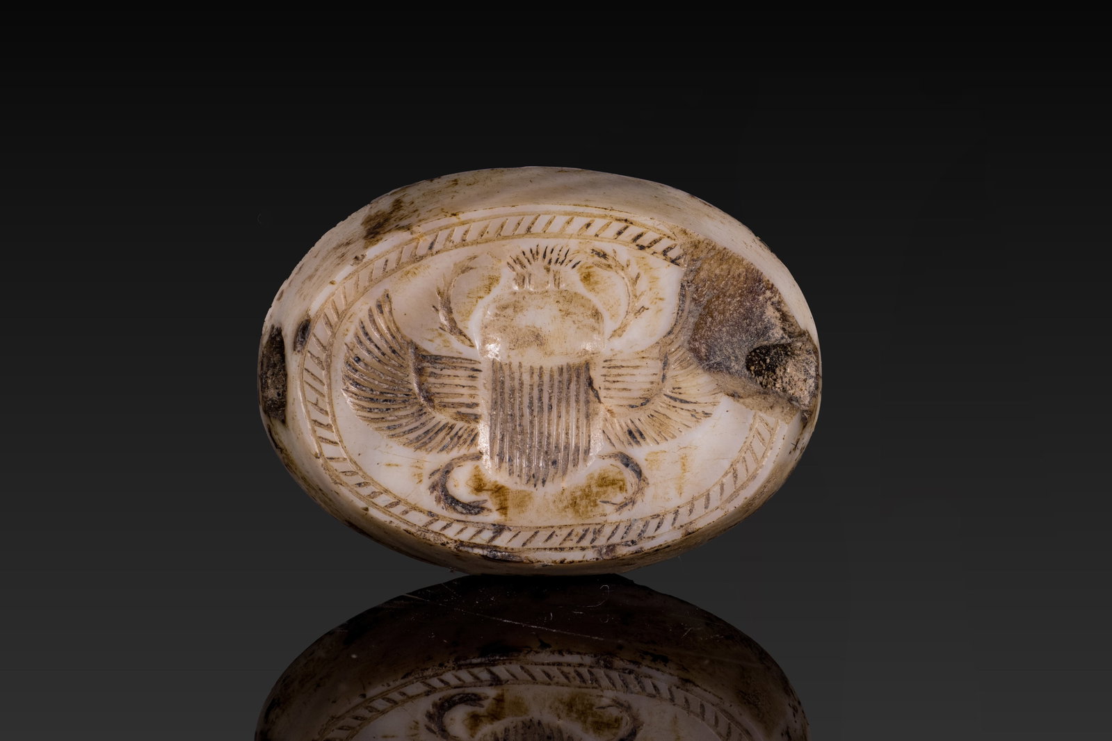 LEVANTINE GRAECO-PERSIAN AGATE SCARABOID: Ca. 700 - 500 BC. A pale agate scaraboid with a smooth convex back, pierced longitudinally through the body. The base is engraved with a large two-winged scarab enclosed by an oval hatched border. Siz