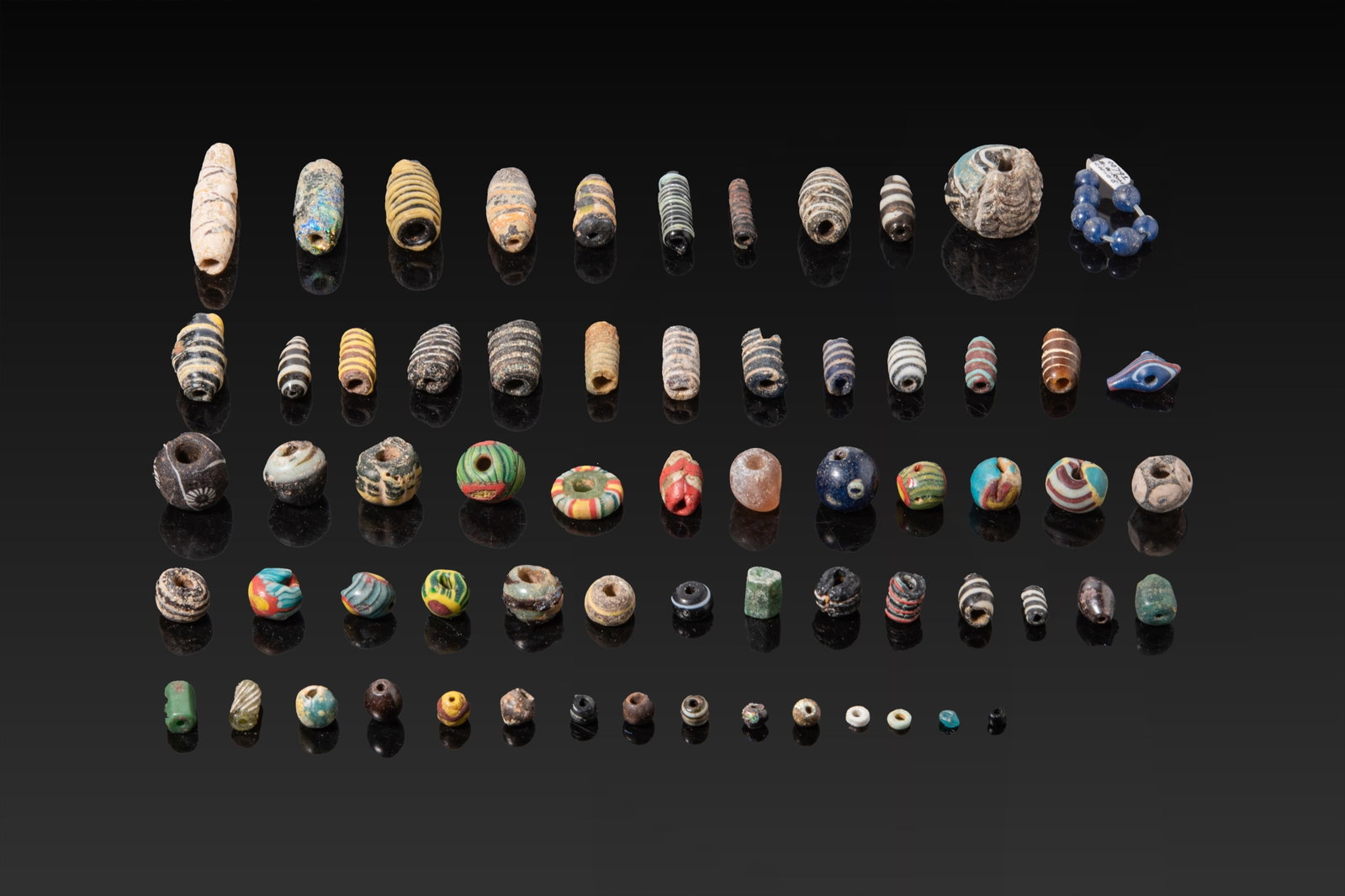 COLLECTION OF GREEK AND ROMAN GLASS BEADS: Ca. 500 BC - AD 200. A collection of polychrome glass beads, comprising rounded, barrel and cylindrical types in varied sizes. The group includes mosaic glass beads and wound glass beads with trailed 