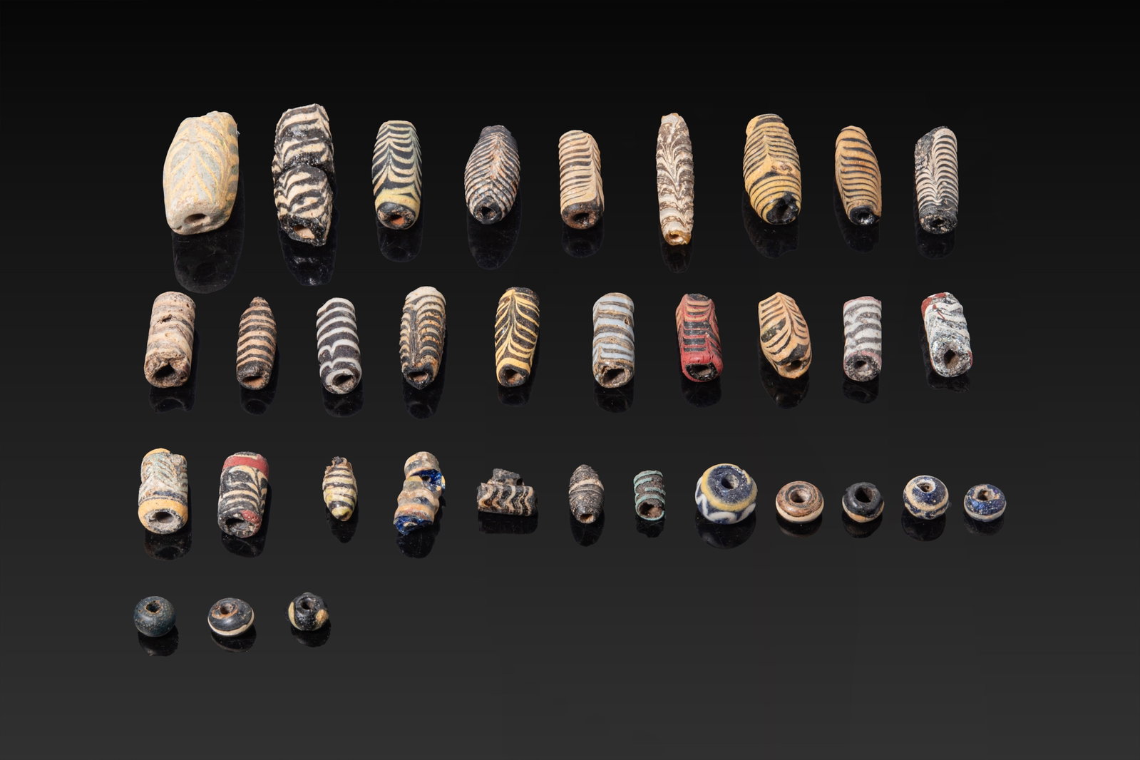 LARGE COLLECTION OF GREEK CORE-FORMED GLASS BEADS: Ca. 400 - 200 BC. A large collection of polychrome glass beads, comprising cylindrical, barrel and rounded types in varied sizes. The group includes core-formed glass beads with trailed and combed dec