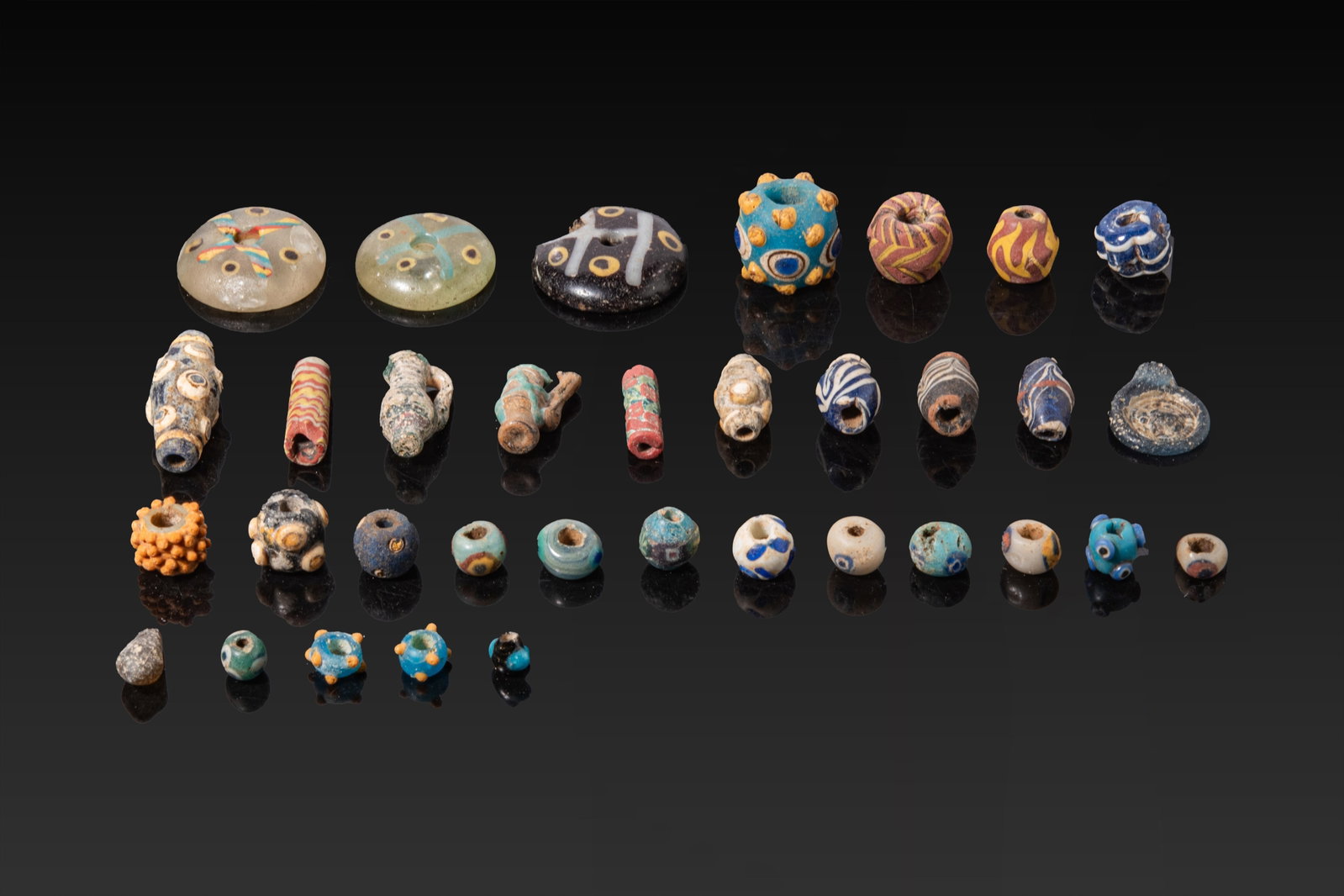 LARGE COLLECTION OF PHOENICIAN, GREEK AND ROMAN GLASS BEADS: Ca. 600 BC - AD 200. A collection of polychrome glass beads, comprising disc, barrel, tubular, jug-shaped and rounded types in varied sizes. The group includes beads with applied concentric eyes, rais