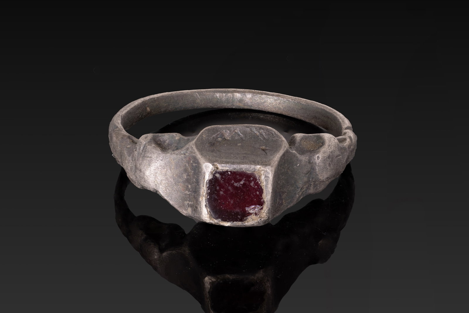 MEDIEVAL SILVER RING WITH RED GARNET: Ca. AD 1200 - 1400. A silver ring with a slender rounded hoop expanding into angular shoulders flanking a square mount with a red garnet. Size: D:17.12mm / US: 6 3/4 / UK: N; Weight: 3.5g Provenance: 
