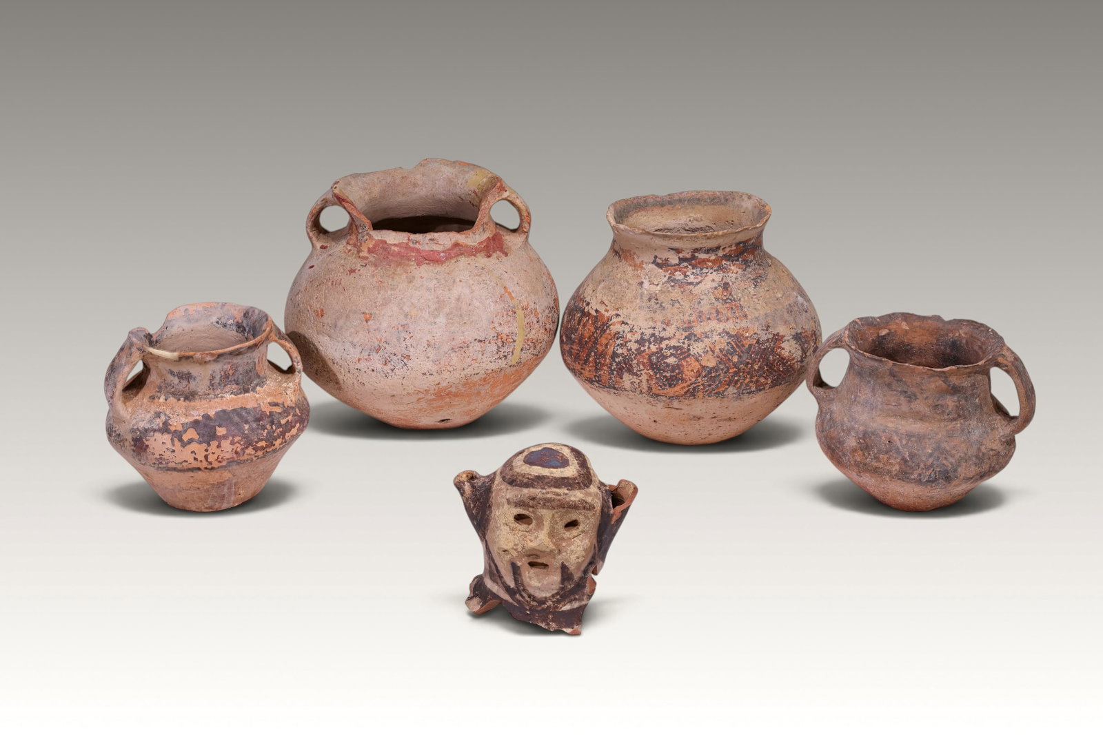 GROUP OF FIVE CHINESE MAJIAYAO POTTERY VESSELS: Neolithic period, ca. 3300 - 2050 BC > A group comprising four small double_looped painted pottery jars and one painted terracotta human head sculpture. The jars are decorated with faded painted geome