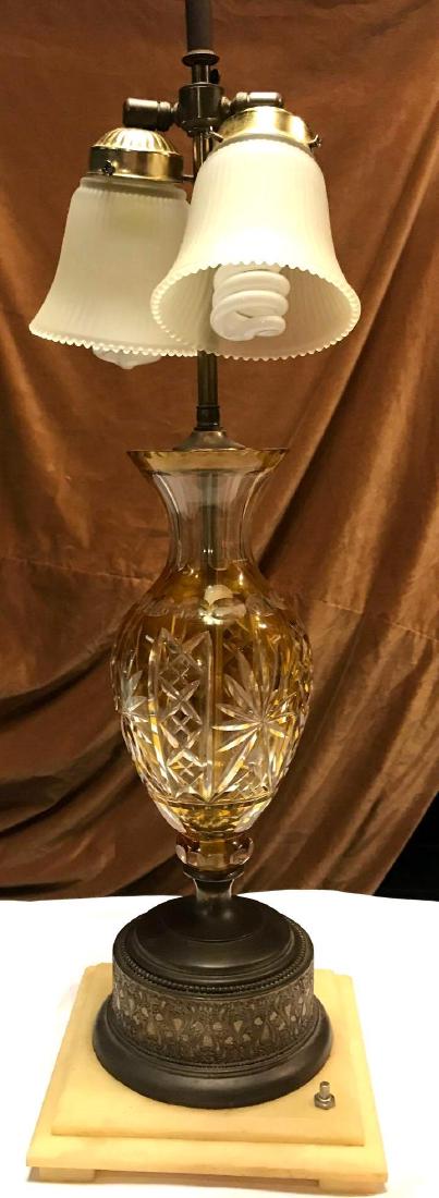 Antique Cut Amber Clear Glass Lamp: One antique amber cut clear crystal like table lamp with star pattern. It has a brass base atop a larger marble base. It is a two socket light with frosted glass globes. Measures Approx. 29" high to f