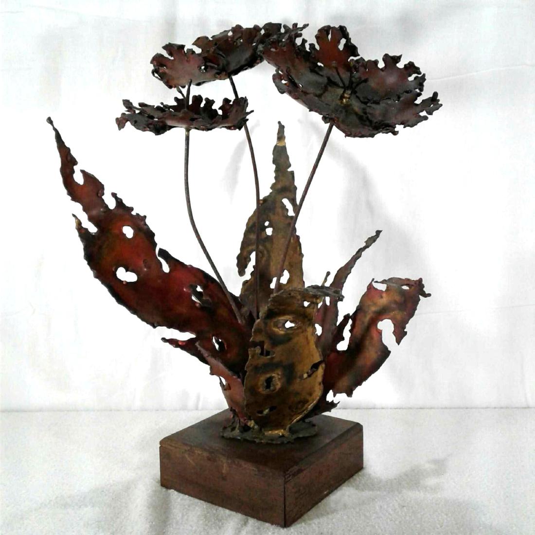 "Silas" Copper Flower Mid Century Sculpture: A signed "Silas" brass flower plant on wooden stand. One leaf is loose and need to be reattached. Measures approximately 17" x 12" and is in good used condition. There are no other known signs o