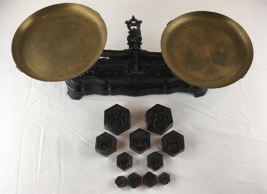 Antique Force 10 Kilo Scale with 11 weights: Antique black cast iron weighted 10 Kilo scale measured at 10 1/2" H x 17 1/2 W x 5' deep with brass platters measuring 8 5/8" . 11 weights including 2 Kilo, 3 Demi Kilo w/ rings, 2 Hectoand 2 1/2 Hec
