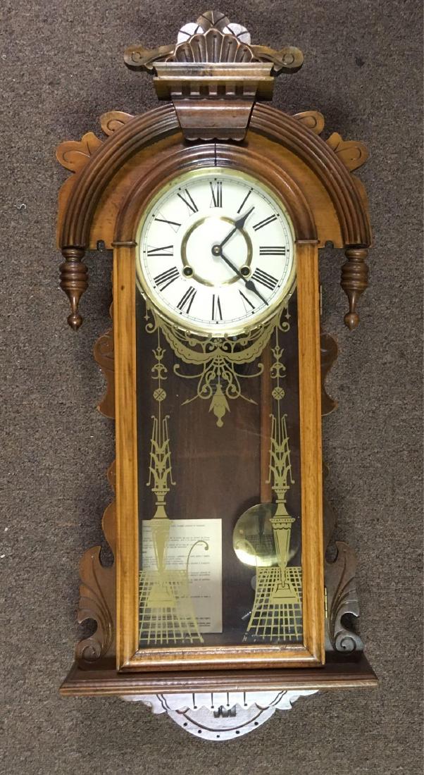 German Wooden Wall Clock: Vintage German Wooden Wall Clock; This piece has ornate wooden fixtures atop and bottom and a glass door with golden embellishments. It includes the key and winds fine, however when turned the pendulu