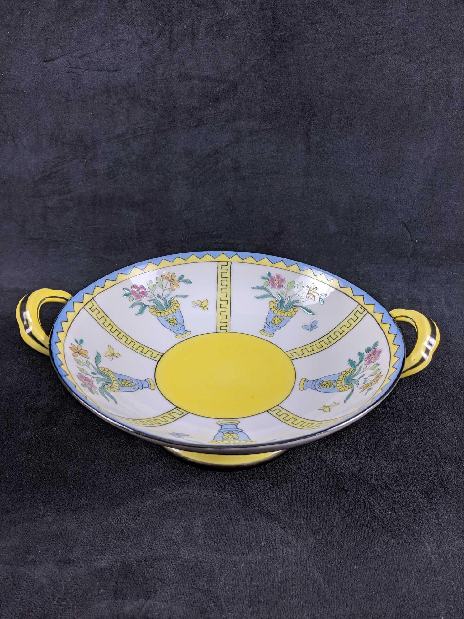Vintage Noritake Footed Bowl with 2 handles: Vintage Noritake Footed Bowl with 2 handles. This bowl is white,yellow and blue and features a design of some flowers inside a vase. There are no known chips or cracks on the bowl or handles and is in