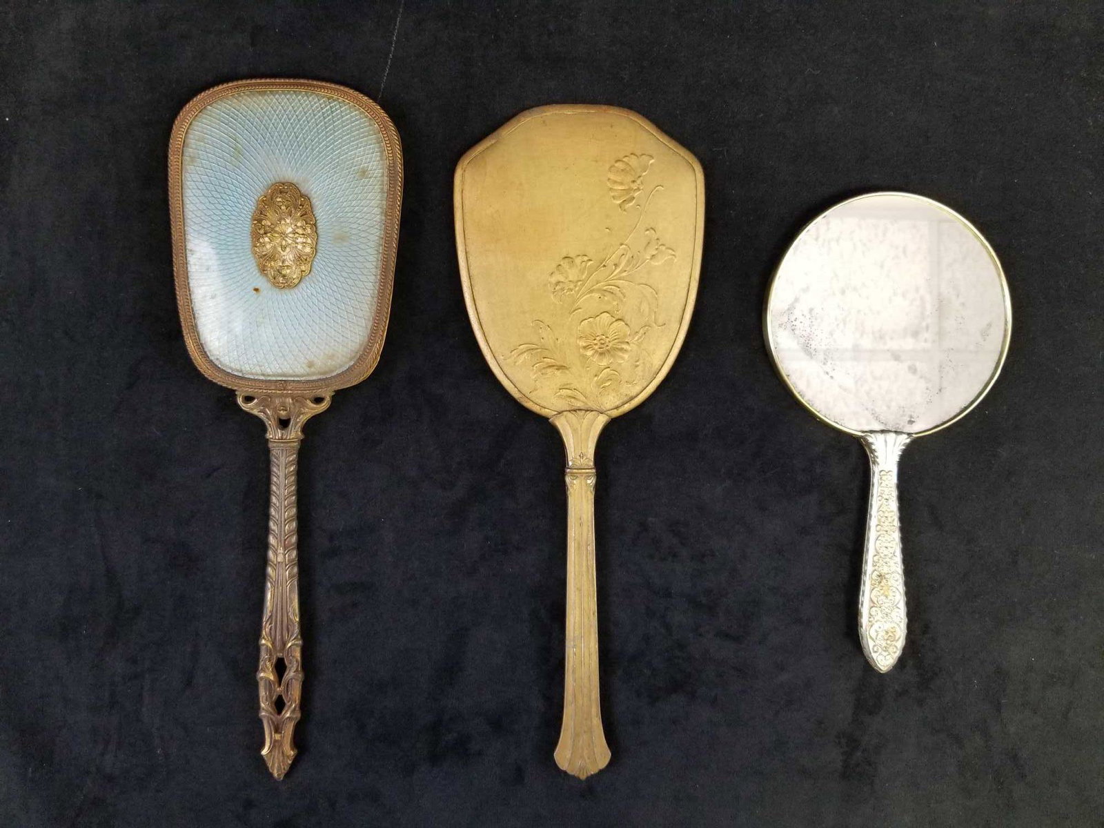 3 Vintage Handheld Mirrors: This lot of vintage mirrors consists of 1 brass mirror measuring about 14" with a beautiful vine detail; a 9" "silver" mirror made in Japan from an unknown material; a solid metal, brass colored 13" m