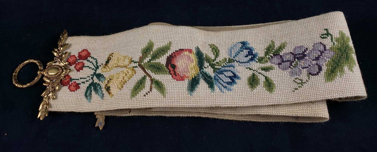 Floral and Fruit Needlepoint Table Runner: Floral and Fruit Needlepoint Table Runner. This table runner is in good condition. It has some discoloration which may be removable through cleaning. The table runner has two bronze decorative ends. M