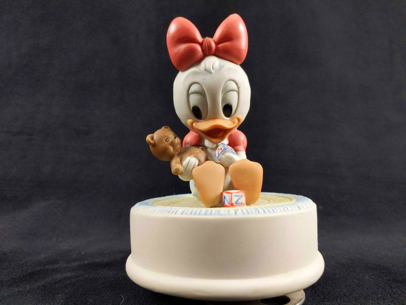 1984 Baby Daisy Duck With Teddy Bear Music Box Figurine: 1984 Goebel Disney Babies Daisy Duck "Toy Island" Music Box. Music Box is in working condition. Daisy's teddy bear appears to have been repaired and has a hairline fracture from it being glued back to