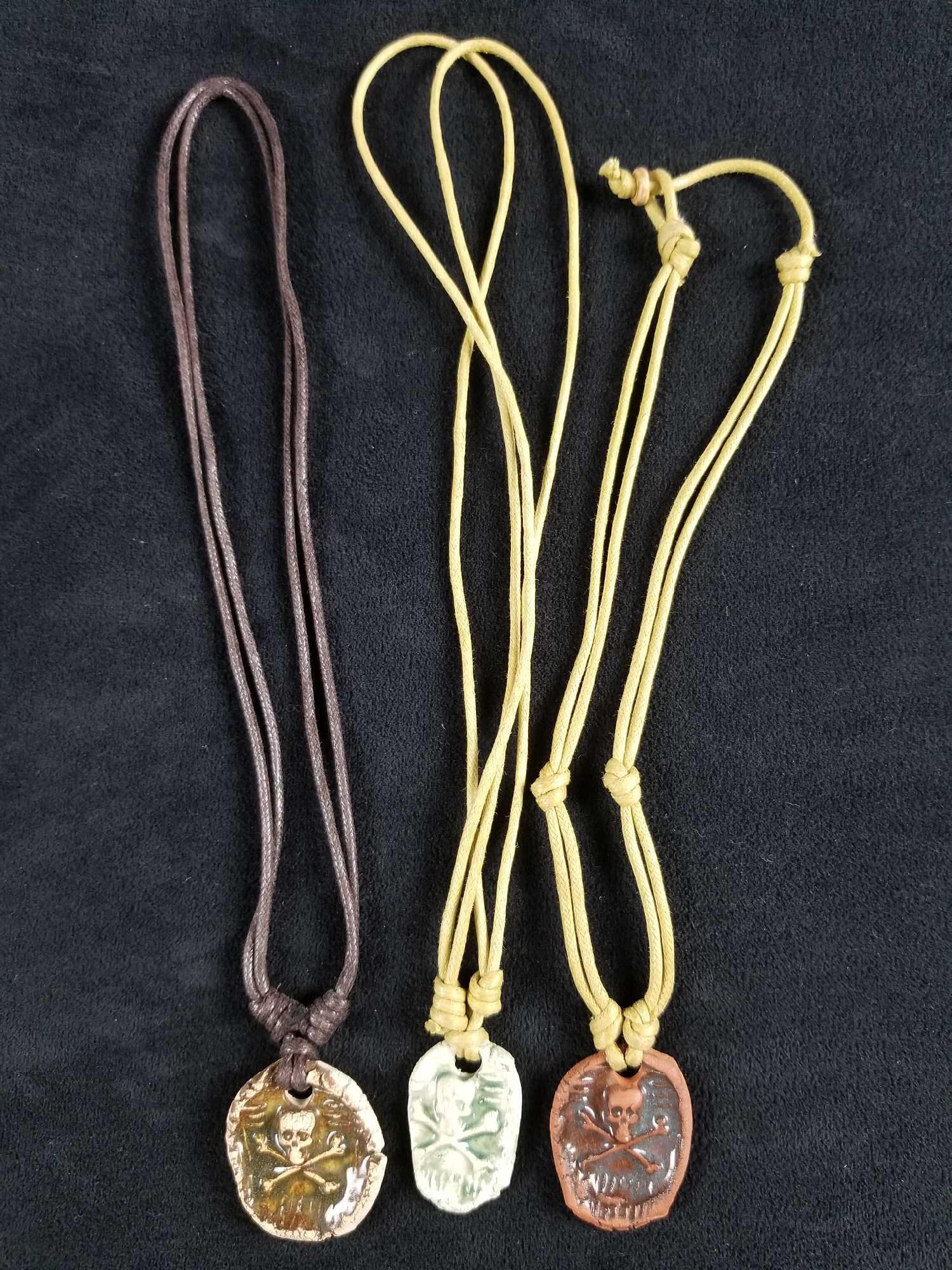 Set of 3 Pirate Skull and Bones Necklaces: This set of 3 Pirate Skull and Bones Necklaces consists of one green, brown and red clay colored pendants made from pressed clay with a strong rope tie. Each pendant measures approx 1 1/2" x 1 1/4" wi