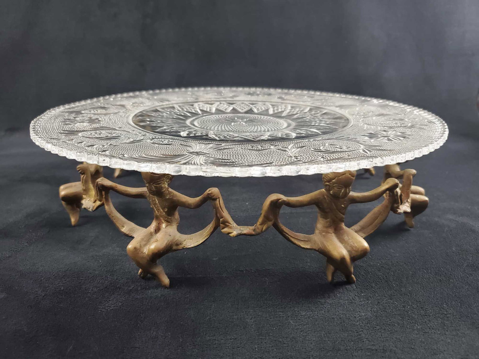 Vintage Centerpiece Glass Platter W Brass Cherubs: Vintage glass platter with an interesting brass circle stand of cherubs that hold the glass plater. Platter has an unique sun and floral design. Is approx 13" x 13" x 3". Glass is in good, vintage con