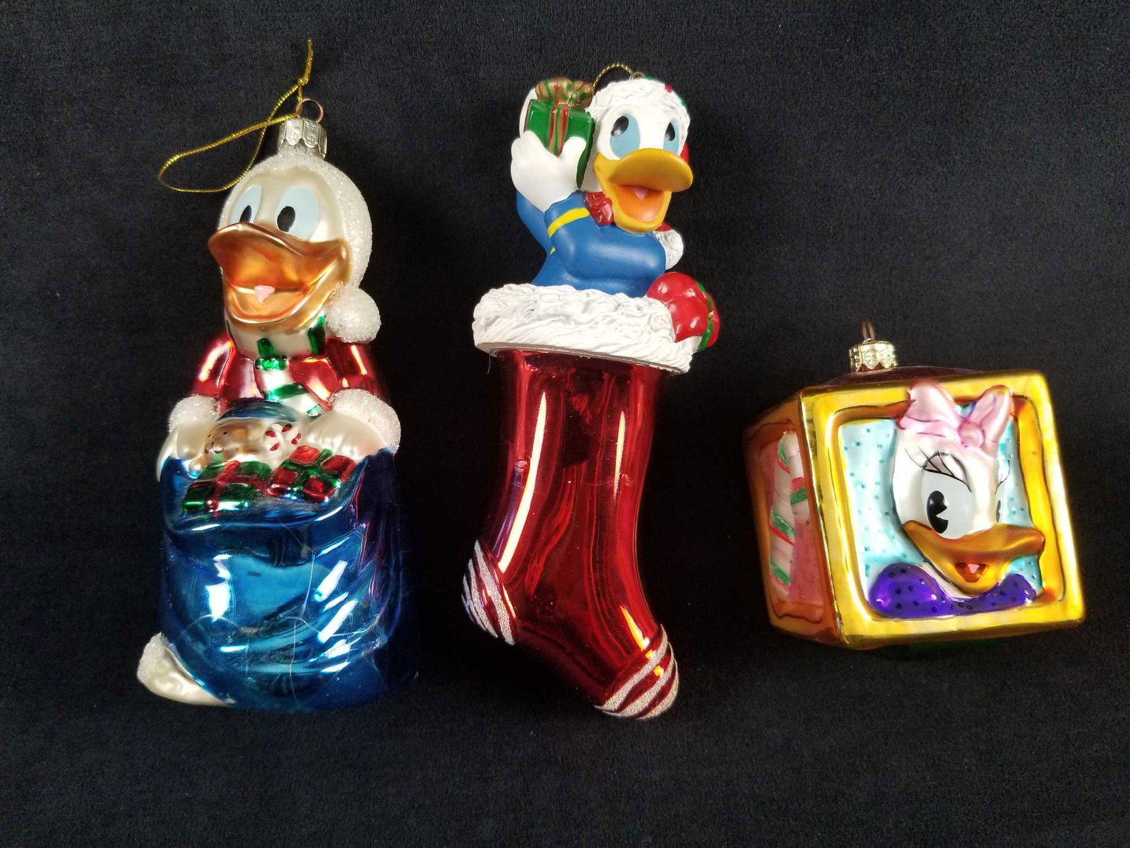 Disney Radko And Radko Like Christmas Ornaments: This lot includes three Radko and Radko-like glass Christmas ornaments. Included: Donald Duck with bag, Donald in stocking with gift, and Donald and Daisy Duck in glass box. All are in 
