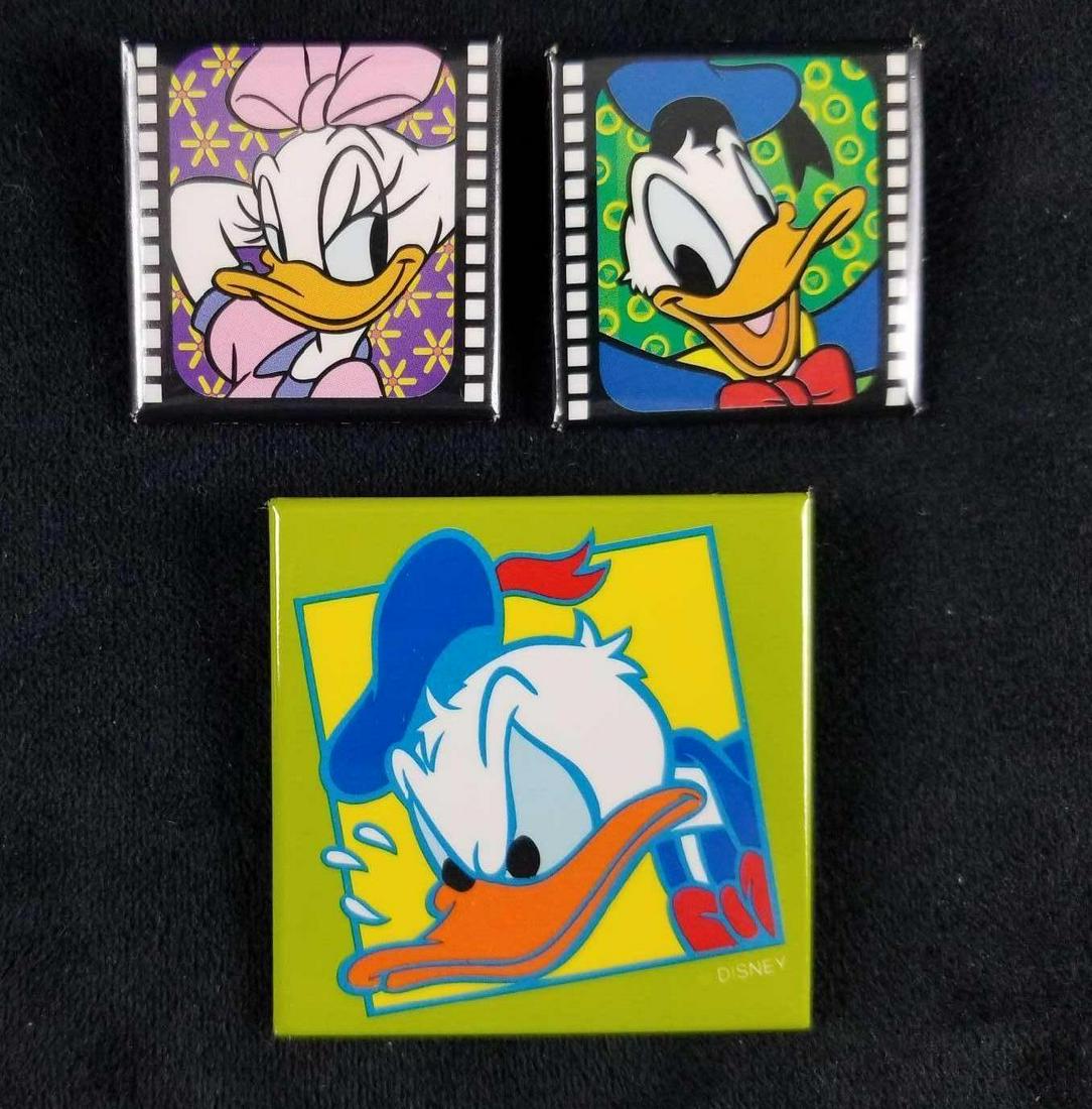 Disney Square Lot Of Three Donald And Daisy Pins: Lot includes two "Film Strip Donald & Daisy" pins. And angry (Donald) duck pin. All are square pins and are in good used condition with no visible markings. The Film Strip pins are approx 1 1/2" x 1 1