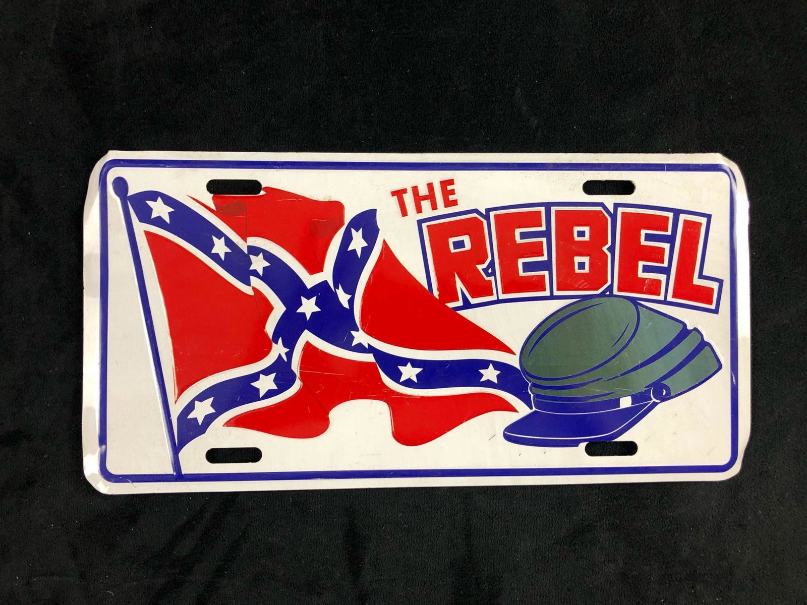 The Rebel Hat Confederate Flag Novelty License Plate: The aluminum license plate depicts the rebel hat and the confederate flag. In good condition with some known scratches. The corners appear to have a slight bend. The cut-out holes are ready for displa