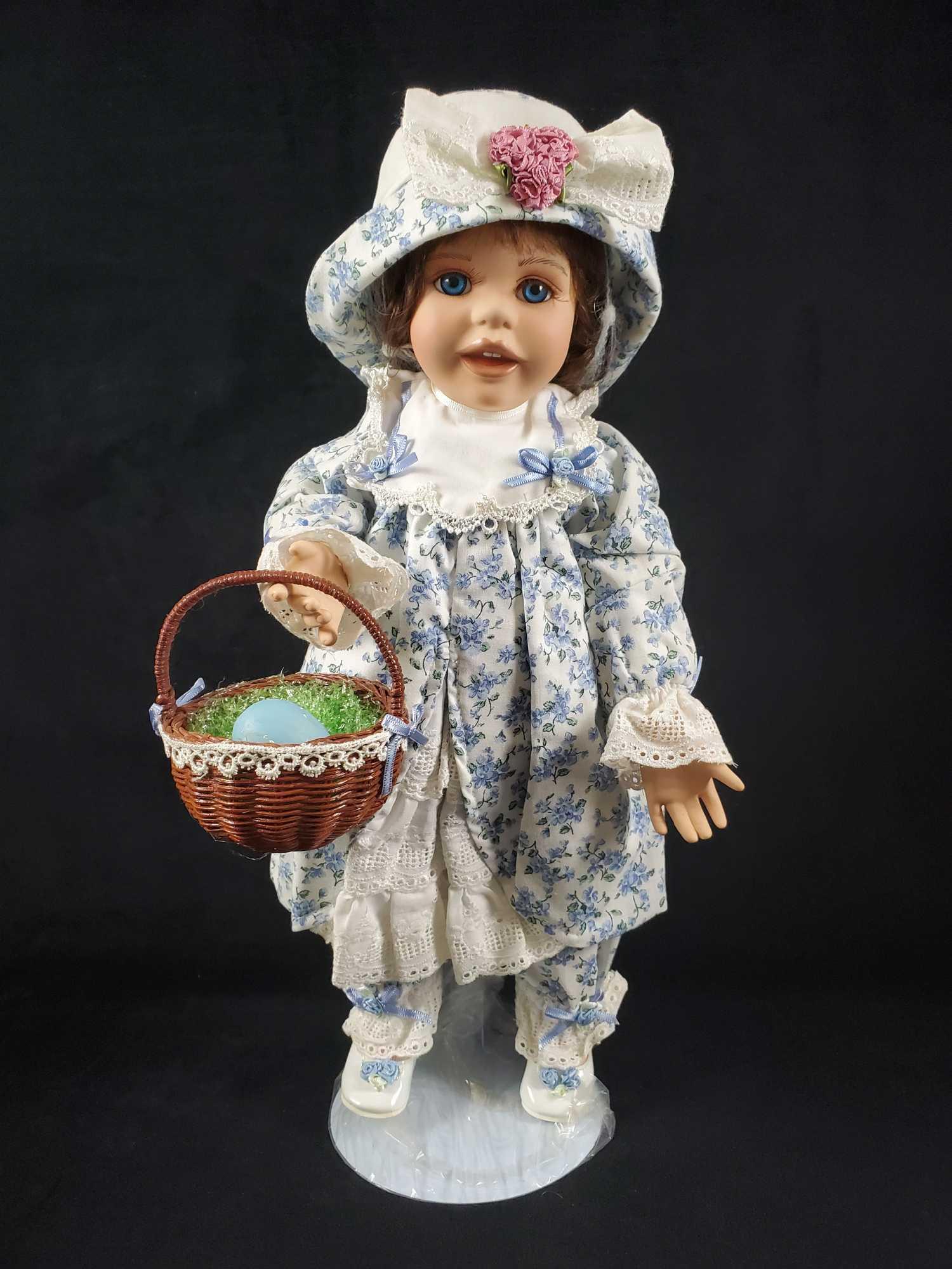 Hamiltons Babys First Easter "Leslie": Leslie's First Easter from the Hamilton Collection. This lovely dolls depicts dark hair, bright blue eyes, a smile- baring teeth and a blue floral dress equipped with a sun hat and Easter basket. She 