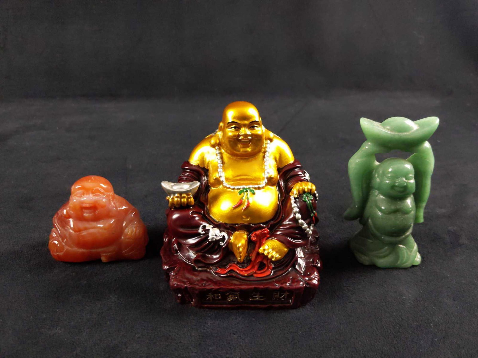 Feng Shui Buddha Figures Lot Of Three: (1) This is a Buddha made out of red stone. It is called red stone because the resin is mixed with Chinese earth material. The gold color is hand-painted. In Feng Shui a Buddha holding an Ingot repres