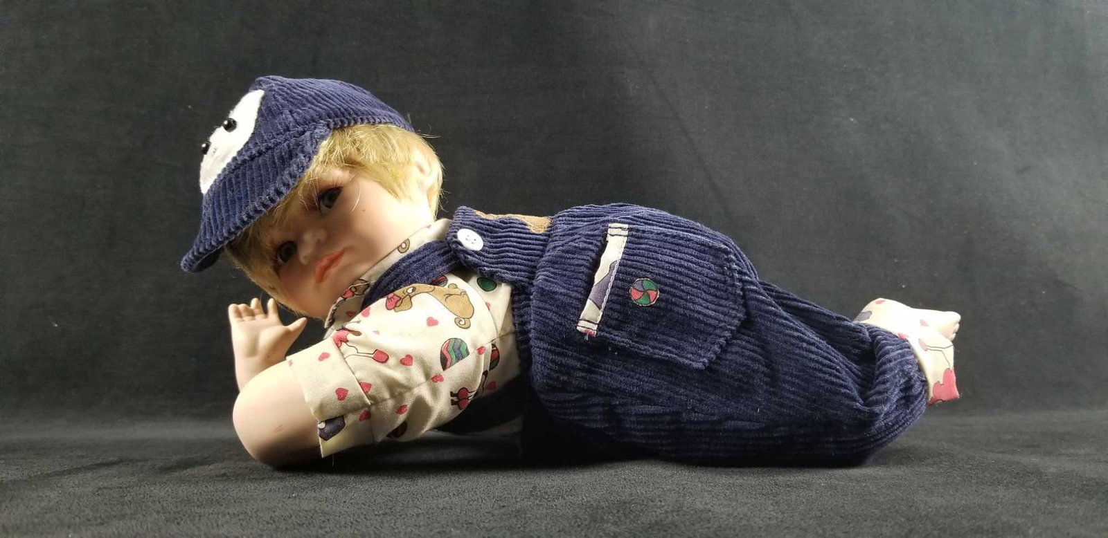Gustave F. Wolff Porcelain Doll 01112 Signed Babyboy In: Vintage Gustave F Wolff "Sammy" Signed # 01112 Porcelain Baby Boy Doll 1998. Baby doll is laying on his stomach in a jumper, shirt and hat that depict puppy dogs. The head, hands, and legs are porcela
