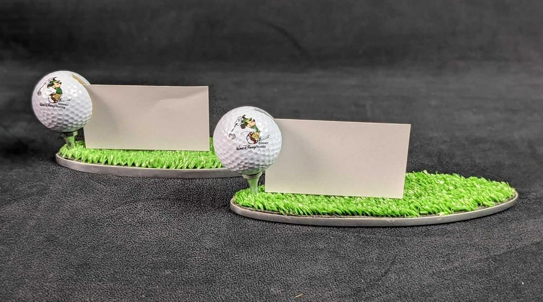 Two Disney Golf Ball Business Card Holders: Two Disney Golf Ball Business Card Holders. With two Mickey Mouse golf balls with a slot to hold your cards and artificial putting green. Is approx 8" x 2 1/2" x 3". Both are in a good, unused conditi