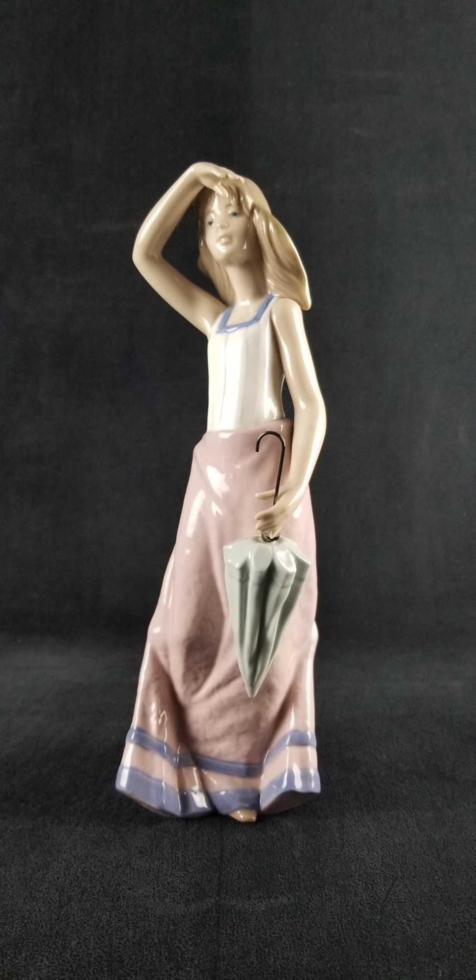 Joven Verano Young Summer Nao by Lladro: Joven Verano "Young Summer" #01294 Summer Girl porcelain figurine is Nao by Lladro. She is tall wearing a white with blue trim tank top and pink with purple trim skirt. She is carrying and umbrella. T