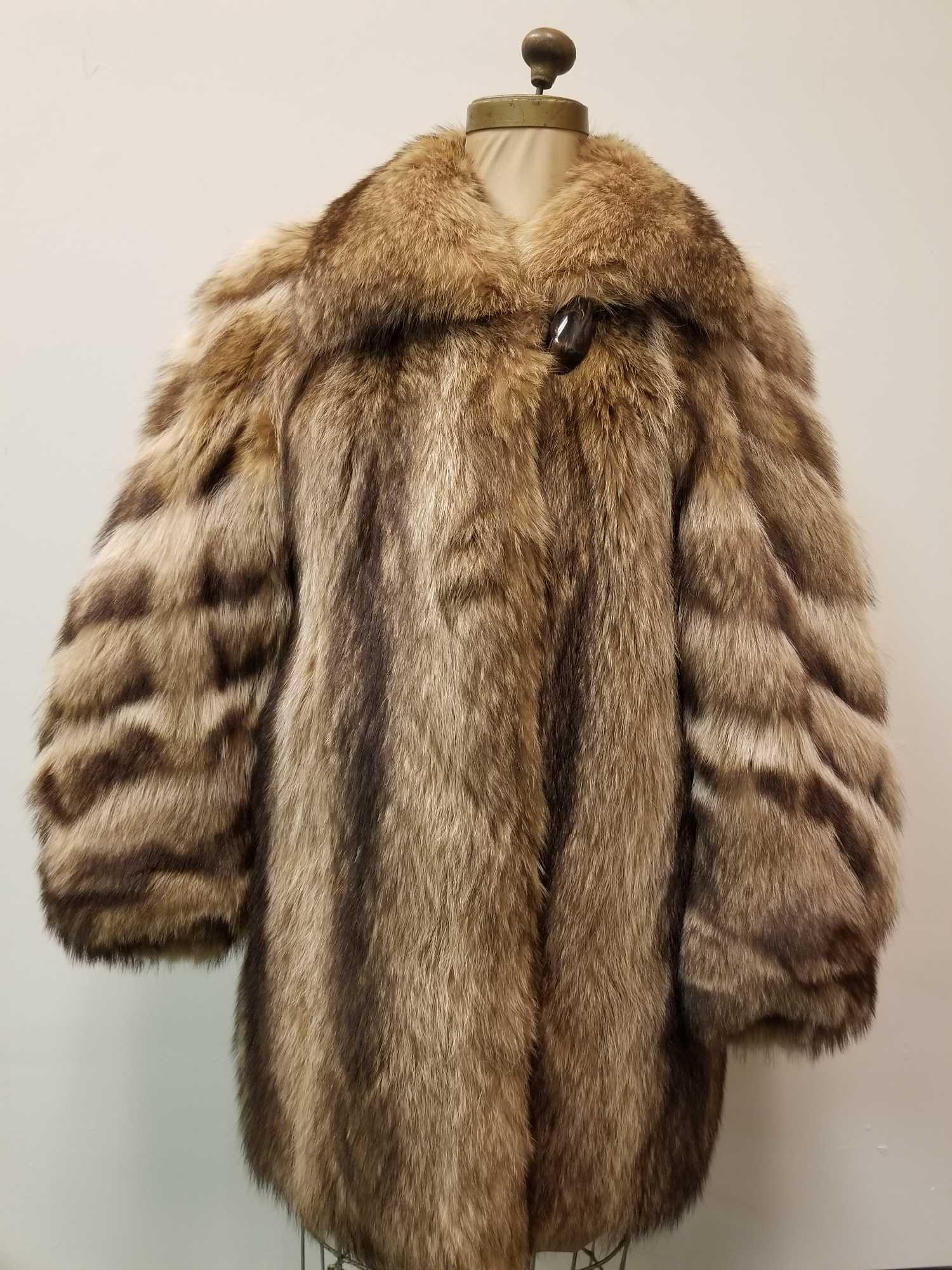 Midlength Raccoon Fur Coat by Designen Furs: This Mid-length Raccoon fur coat by Designen Furs And Leather LTD is in good used condition. This coat has light brown linen interior and what appears to have had an embroidery stich removed (see imag