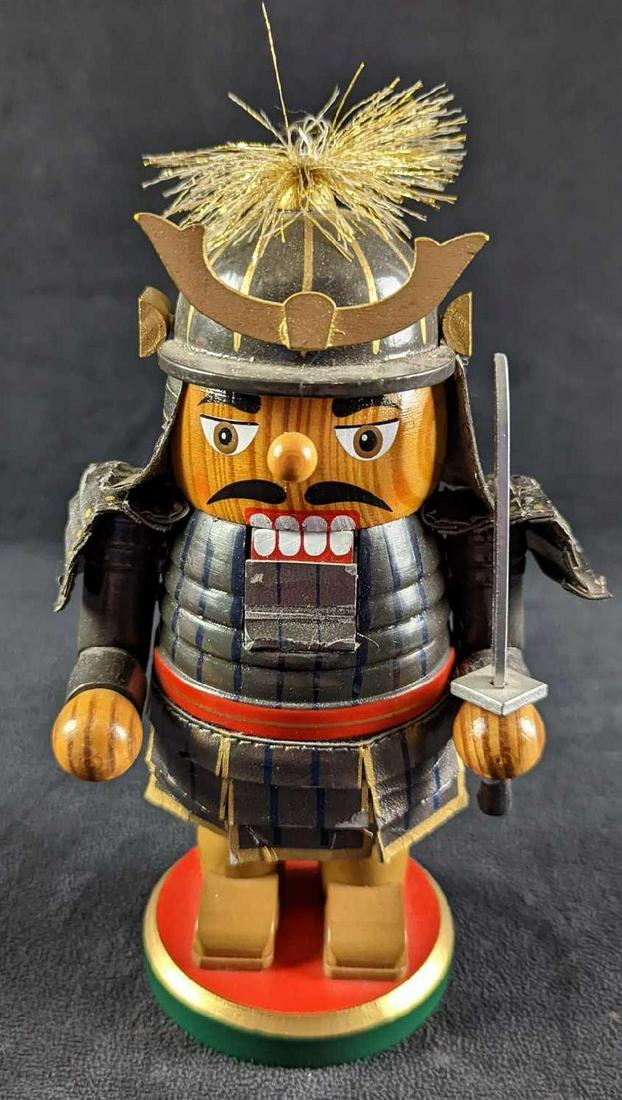 Wooden Samurai Warrior Nutcracker Christmas Holiday: 2010 Samurai with a sword in a gray suit armor with red, blue, and gold trim. It is on a round red, green, and gold base. It is in fair condition, The helmet armor has come loose and the body armor is