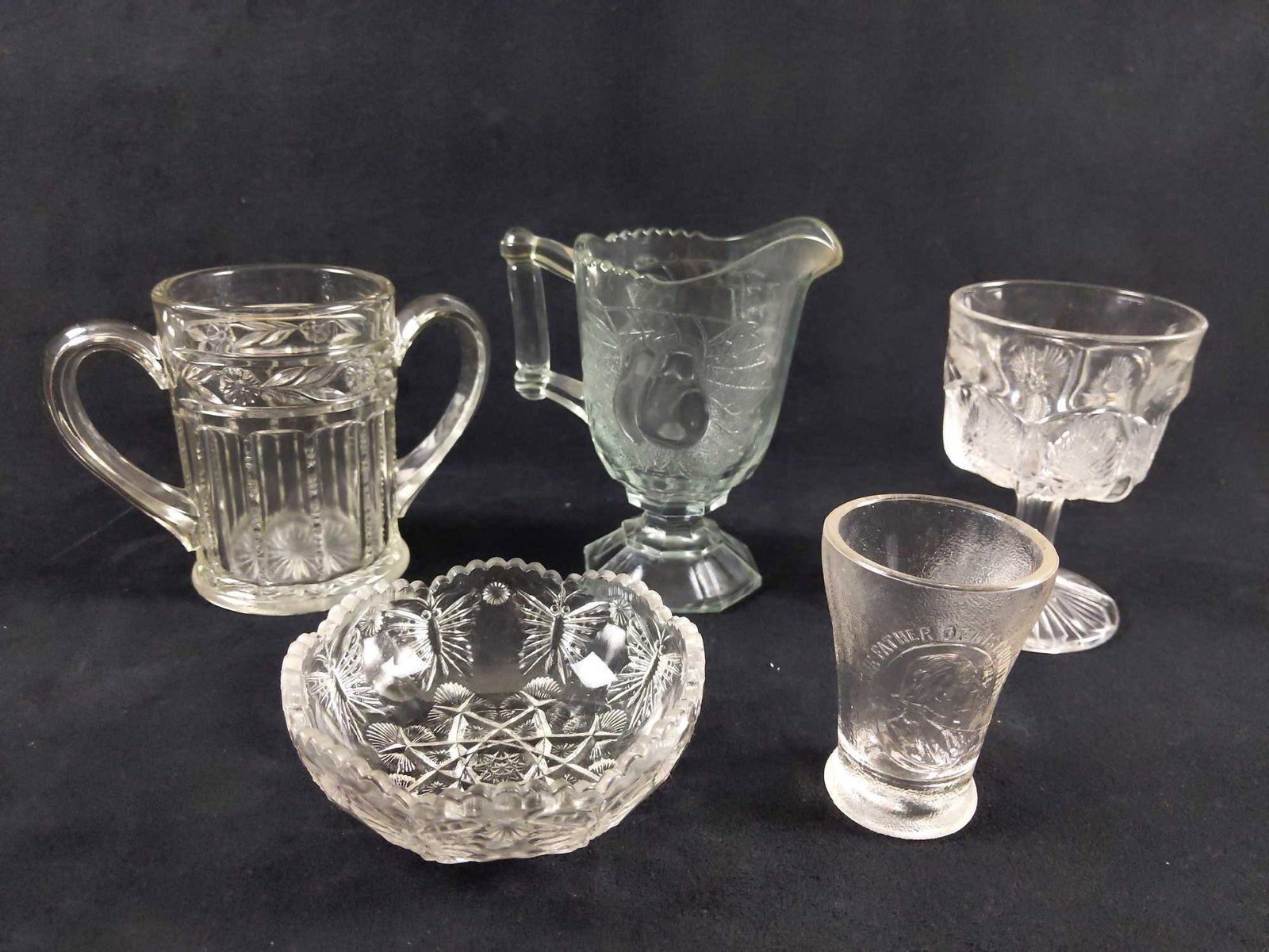 Clear Cut and Pressed Glass Lot of 5: 1) Pressed Glass Clear cup with two handles and a seam that runs along each side. This mug features a floral design around the edge. There are no known chips or cracks on this cup. Cup measures 4"x6".