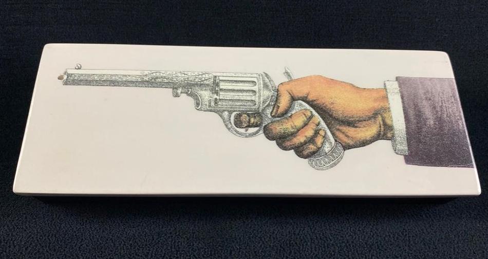 Fornasetti "Pistola" Incense Box: Fornasetti "Pistola" Incense Box Incense box by Fornasetti Profumi. The box is made of dark wood, with a porcelain lid featuring a graphic of a hand holding a pistol. At the end of the barrel, is a sm