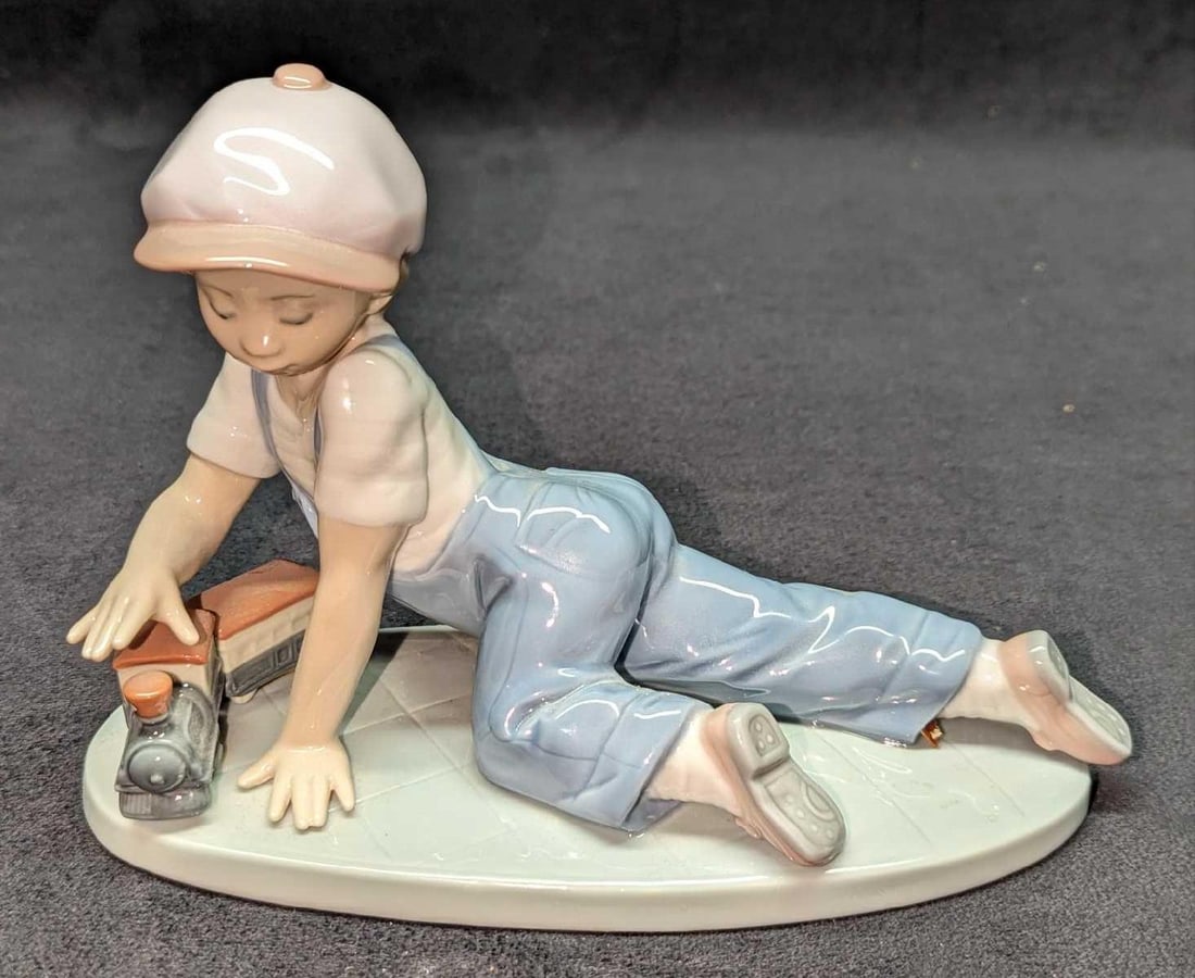 Retired Lladro All Aboard Child With Train Figurine: Retired Lladro All Aboard Child With Train Figurine. This was designed by Antonio Ramos and was released from the year 1992 to the year 1995. This figurine is approx 7" x 3" x 5" and it we