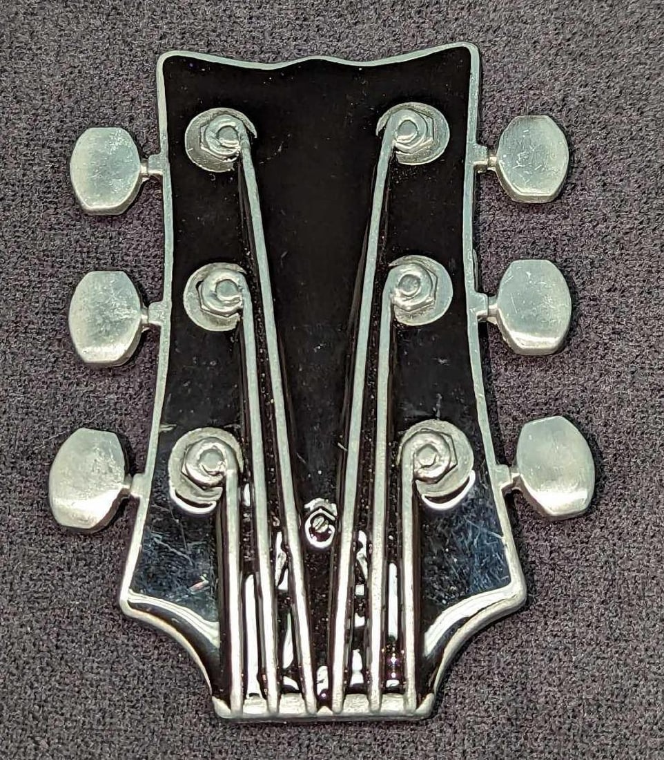 Metal Guitar Headstock Belt Buckle: Metal Guitar Headstock Belt Buckle. Made of an zinc alloy. This belt buckle is approx 4 1/4" x 1/8" x 3" and it weighs 0.25lb. There is some signs of light wear. Its maker and date of crea