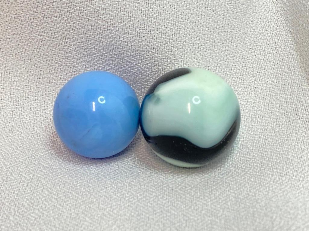 Pair of Vintage Marbles, Maybe Akro & Christensen: Pair of vintage Marbles, 25mm and 22mm in diameter. One is a black and white agate swirl with slight blue hues, and the other is a pale blue with differing shades of swirls. The marbles have a relativ