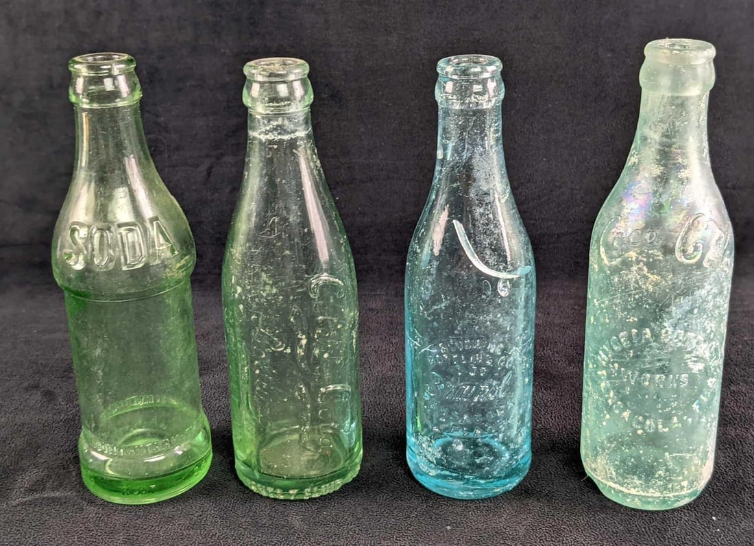 Four Antique Glass Coca Cola Celery-Cola Bottles: This lot consists of: (1) Brainol (Bludwine Bottling, Pensacola Florida). This is approx 2 1/2" x 2 1/2" x 7 1/2". Has sticker residue and some chips and scratches. (1) Early 1900's Coca Bottle. Was b