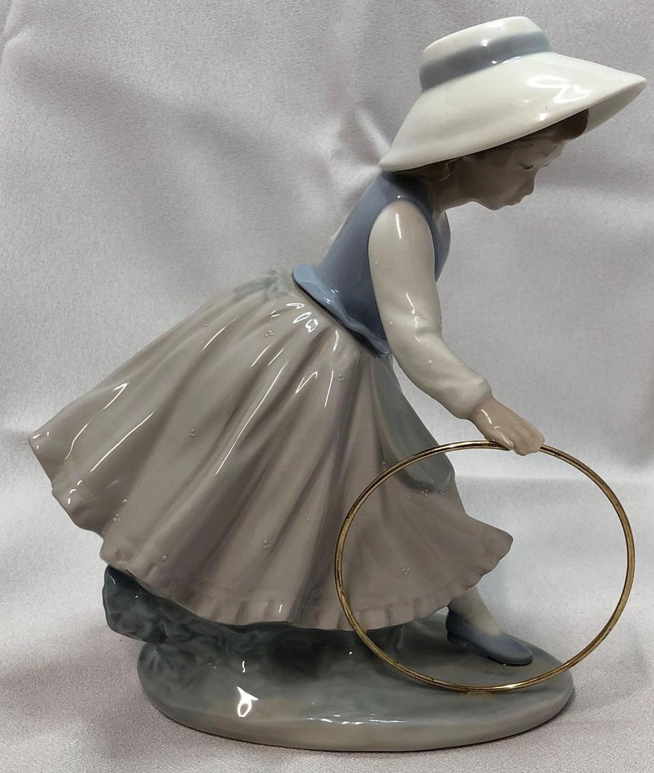 1980 NAO by Lladro 297 Girl With Hoop: This lot contains a 1980 NAO by Lladró 297 Girl With Hoop. It is approx 7-1/2" x 6-1/2" x 4" and it weighs about 2.0lbs. Overall the Lladró is in good used condition with some light wear
