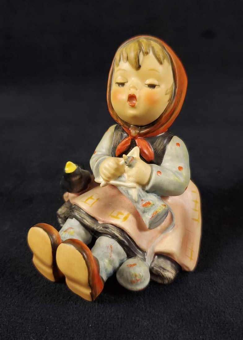 Hummel Goebel Figurine Happy Pastime HUM 69: Happy little Bavarian girl knits away the day as her pet bird watches on. The figure is in good, vintage condition with some sticker residue on the bottom. No chips or cracks. Figure is approx 4"