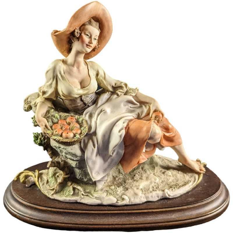 JB Giuseppe Armani Lady Figurine With Apples: Hand-painted Capodimonte porcelain of an woman in peasant dress and hat holding a barrel of apples. The figurine is approx 11" x 5 1/4" x 10 and it weighs 5lbs. The figurine is in a good, vintage cond