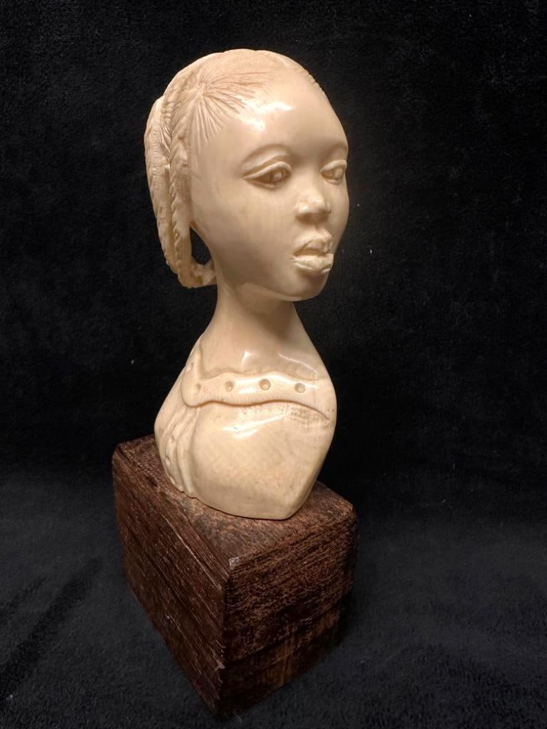 Antique Carved Bone Bust of African Girl: Antique Carved Bone Bust of African Girl Bust of an African girl carved in bone, with detailed braids and face. In very good condition, with a dark wooden block as a base. Approximate size: 7.5"