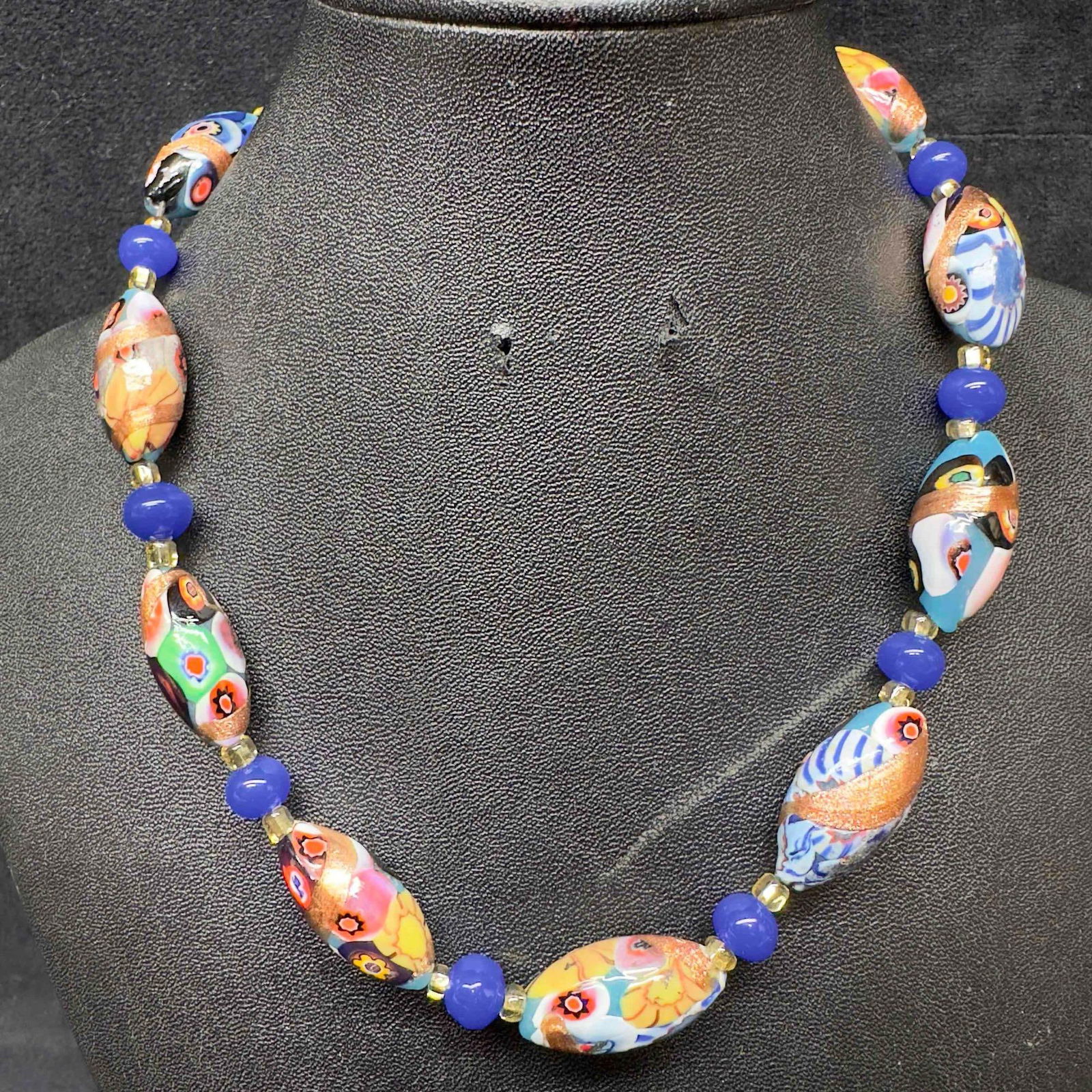 Venetian Murano Lamp Work Art Glass Bead Blue Floral Design Beaded Necklace C44: Venetian Murano Lamp Work Art Glass Bead Blue Floral Design Beaded Necklace C44. Necklace with blue colored glass beads with beautiful designs on each. The necklace features floral accents. The neckla