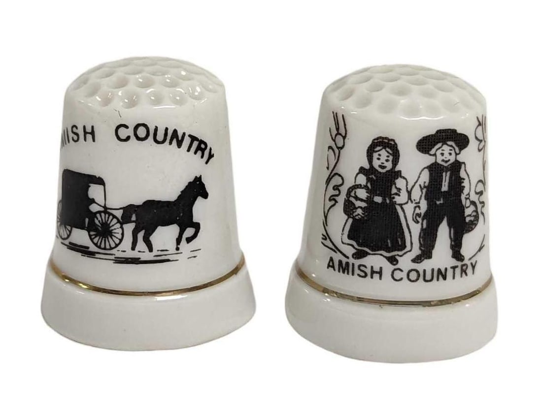 Two Souvenir Amish Country Porcelain Thimbles: Two Souvenir Amish Country Porcelain Thimbles. One thimble shows a man and woman dressed in traditional Amish clothing. The other shows a horse and buggy. Each is approx 7/8" x 7/8" x 1" and together 