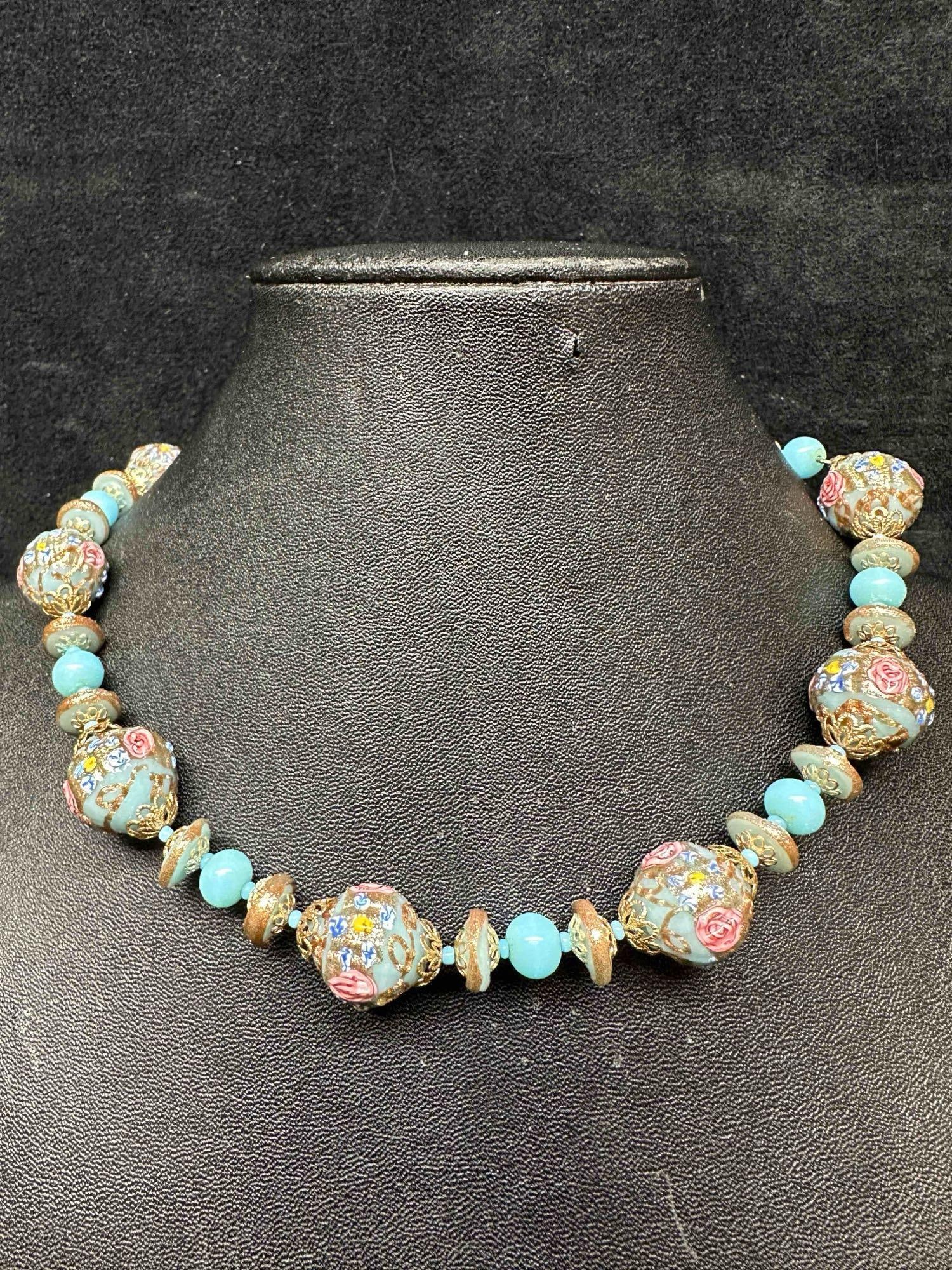 Murano Venetian Lamp Work Art Glass Light Blue Round Floral Accent Beaded Necklace E94: Murano Venetian Lamp Work Art Glass Light Blue Round Floral Accent Beaded Necklace E94. Necklace with light blue colored glass beads with a beautiful design on each. The necklace features pink floral 