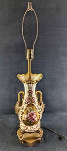 Vintage Gilded Floral Porcelain Table Lamp: Vintage Gilded Floral Porcelain Table Lamp. This lamp looks like it was converted from a regular vase. Sits upon a brass-toned stand with cupids. The lamp is approx 8" x 8" x 34" (without the harp, it