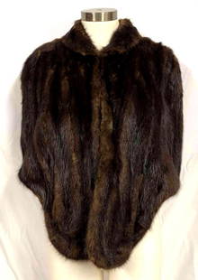 Mink Dyed Muskrat Fur Cape By La Belle Fine Furs Since 1919: This lot contains a mink-dyed muskrat fur cape by La Belle Fine Furs Since 1919 Orlando- Daytona Beach-FLA. This cape features two exterior pockets for storage, two hooks and loops for closure, and a