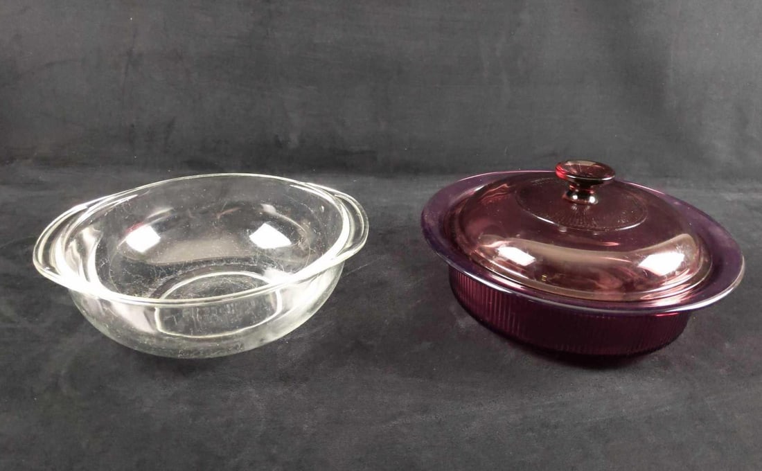 Two Pyrex And Vision Glass Cookware: This lot includes: (1) Clear Pyrex Glass Bowl With Handles. Safe for the oven. Is approx 10" x 10" x 3". Has small scratches between glass. (1) Vision Cranberry Colored Glass Bowl With Li