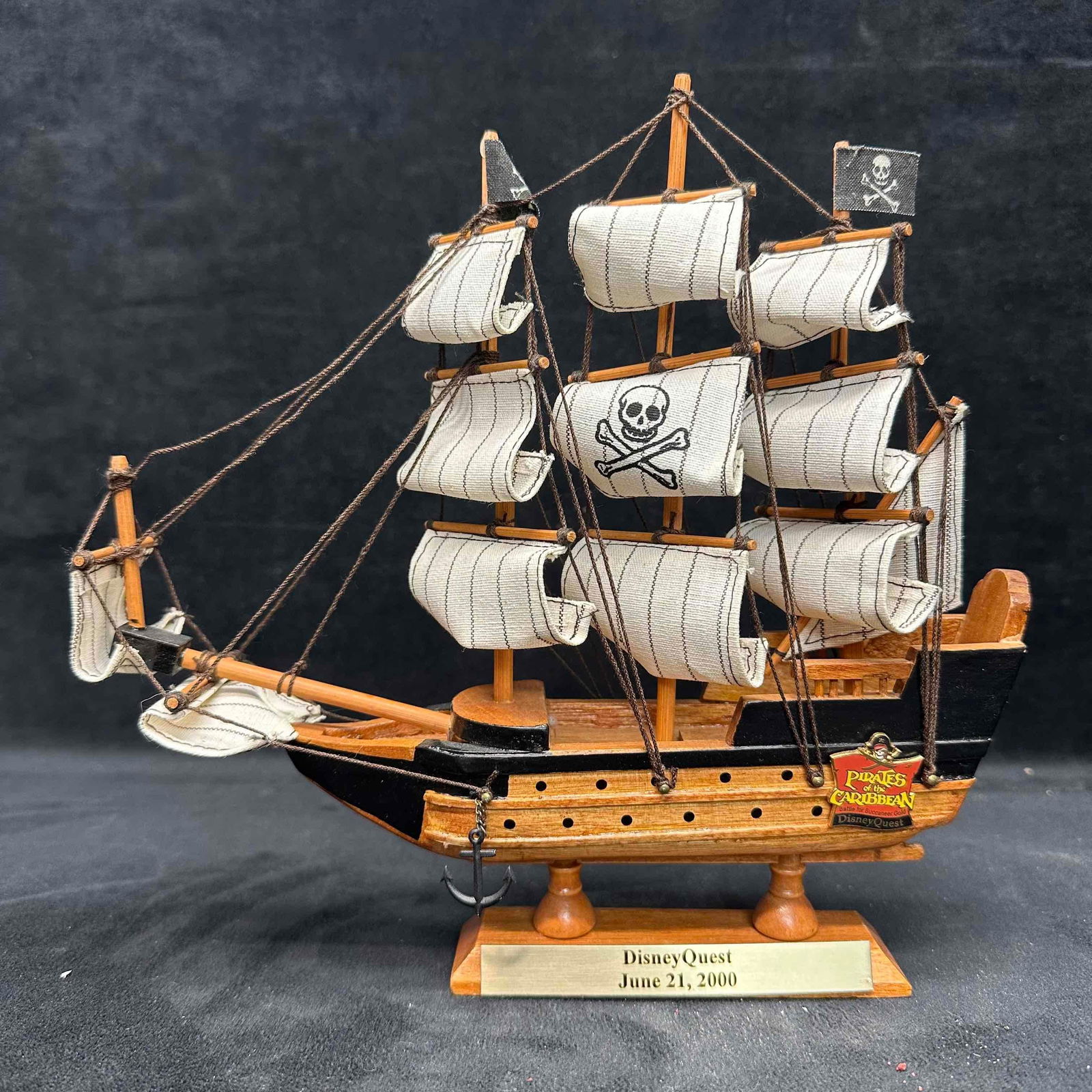 DisneyQuest Pirates of the Caribbean Battle for Buccaneer Gold Ship Model and Disney Pin: Wooden display model ship with cloth sails and skull-and-crossbones design, commemorating the Pirates of the Caribbean: Battle for Buccaneer Gold attraction at DisneyQuest. Features brass plaque readi