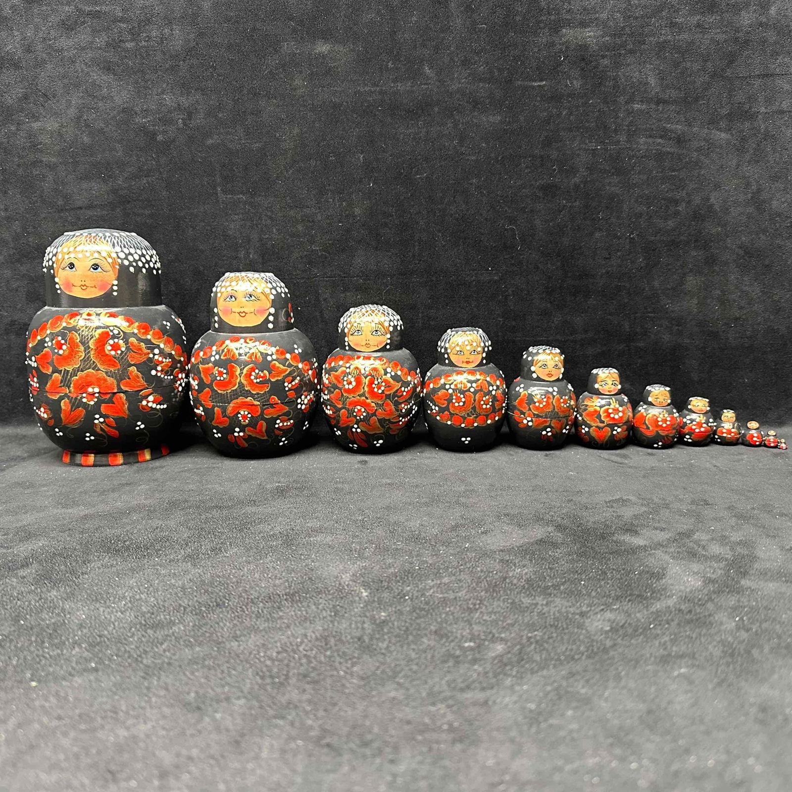 Large Set of 12 Hand Painted Russian Nesting Dolls Black with Red Gold Floral Design: Hand-painted Russian nesting dolls featuring a striking black background with red, gold, and white floral accents. This complete set includes twelve dolls, each fitting inside the next, with the large