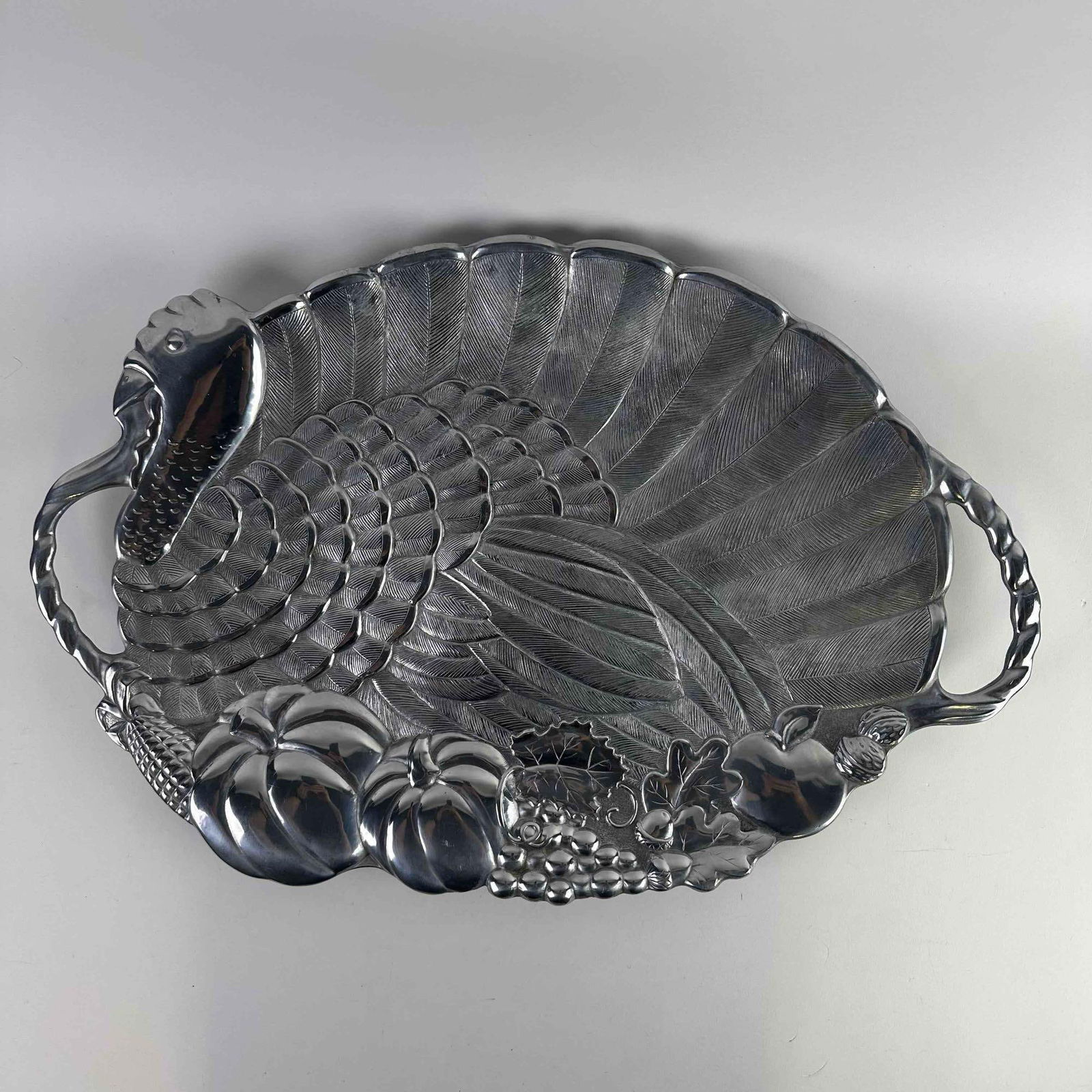 Gorham 1831 Large Turkey Serving Platter Metal Holiday Serveware: This is a decorative Gorham metal serving platter shaped like a turkey, featuring detailed feather textures and harvest-themed elements including pumpkins, corn, and grapes. It has handles on each sid